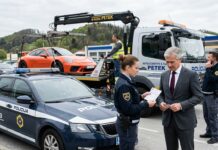 Odvzem vozila, zakaj naknadna „prodaja” avta ne deluje in kaj lahko naredite drugače Police car in the foreground as a tow truck hauls an orange sports car; a policewoman hands paperwork to a suited man while another officer talks on a mobile phone nearby.